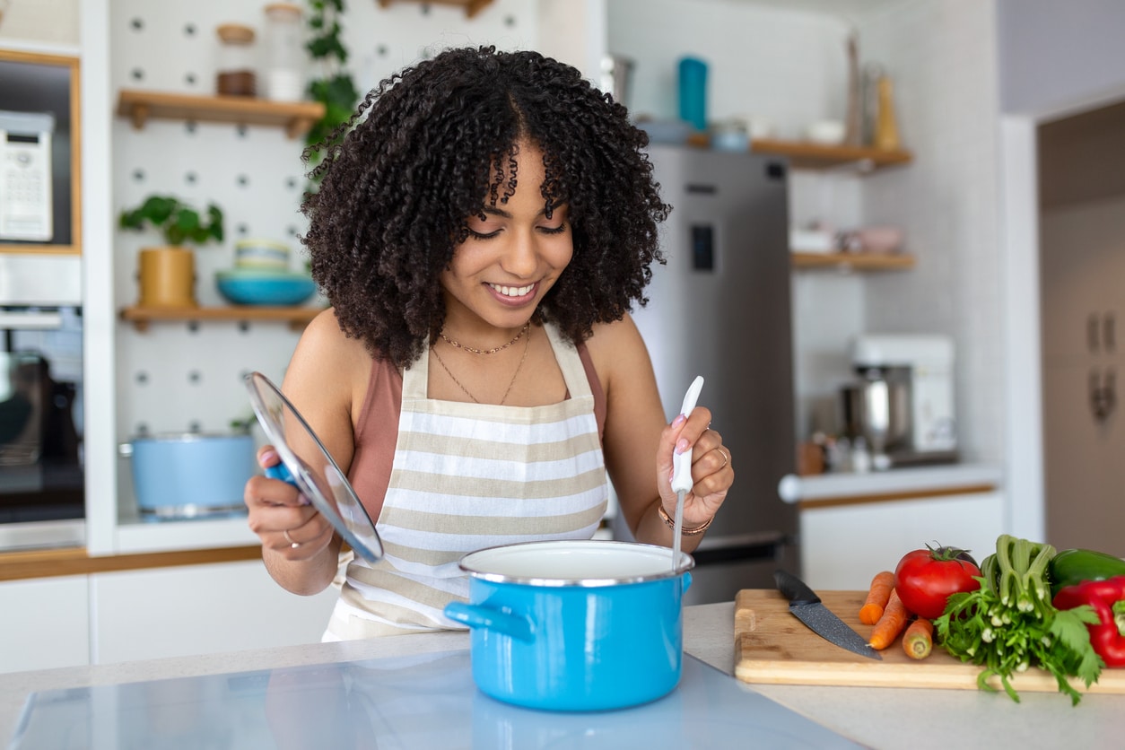 A young woman with curly hair cooking in a kitchen.