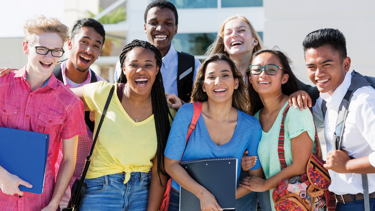 A diverse group of high school students taking selfie in front of school building.